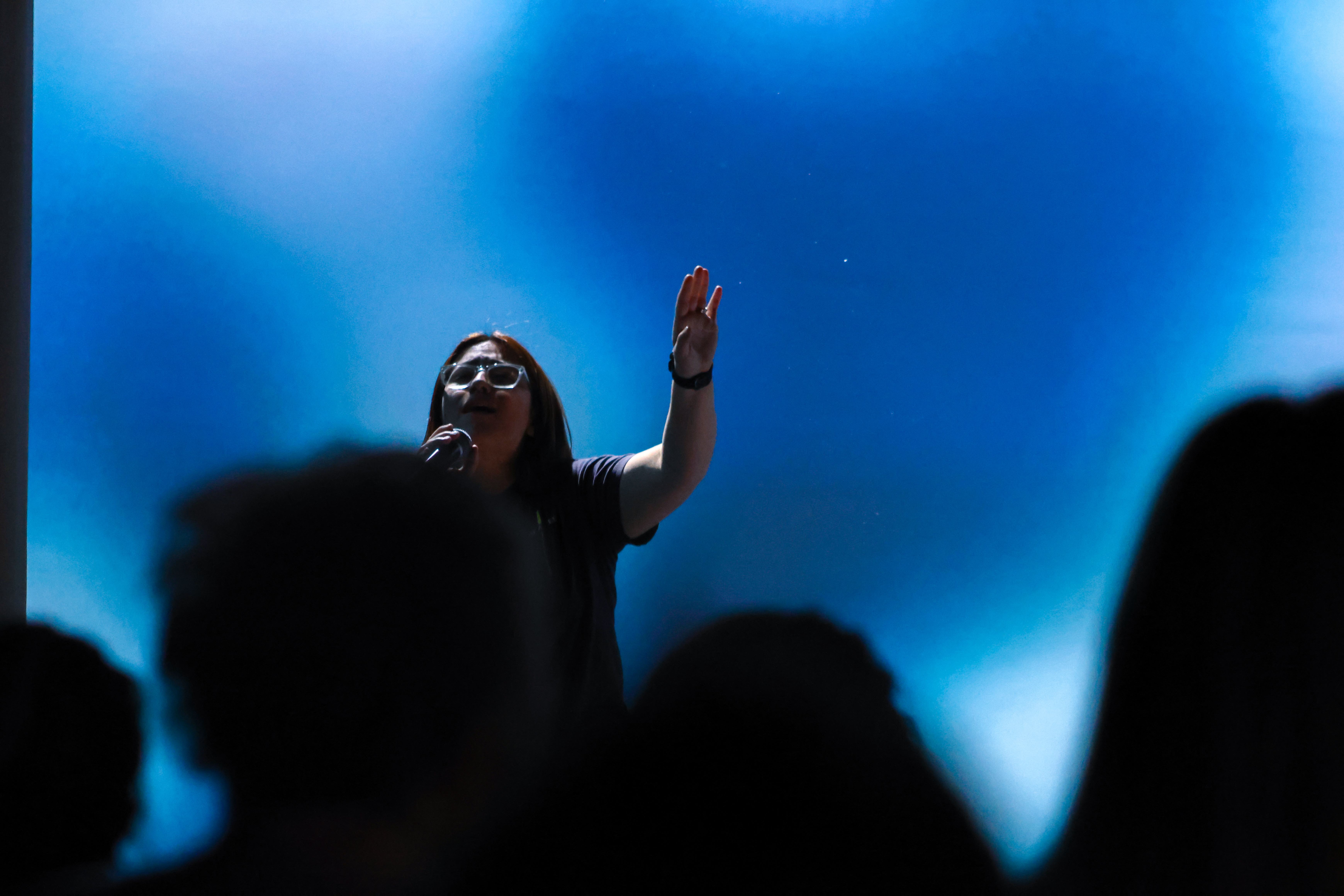 Woman worshipping with a raised hand under blue stage lighting at Ethos Church