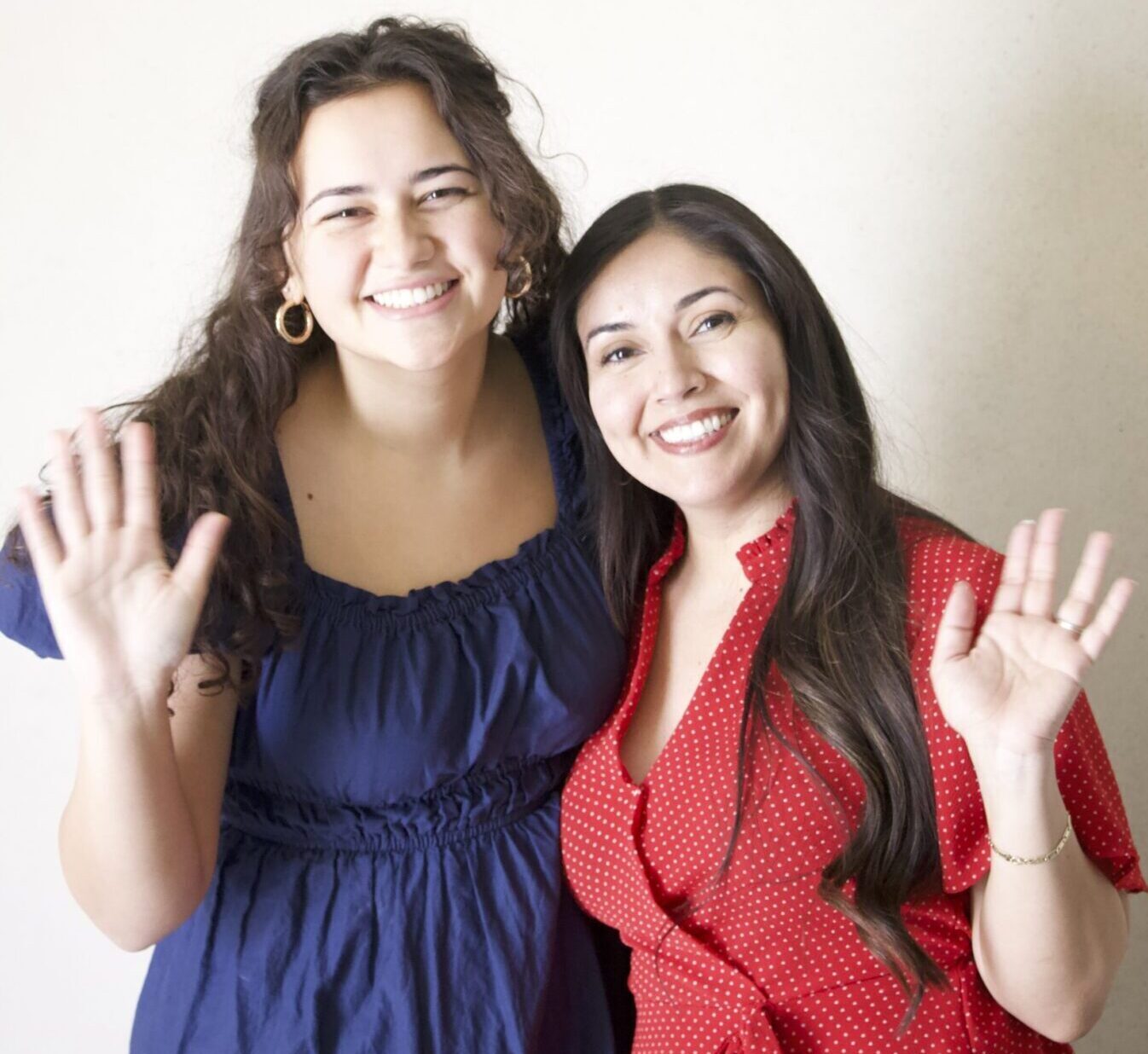 Two women standing next to each other and waving.